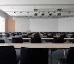 PROYECTOS Spacious contemporary conference room with rows of tables and chairs, ready for meetings.